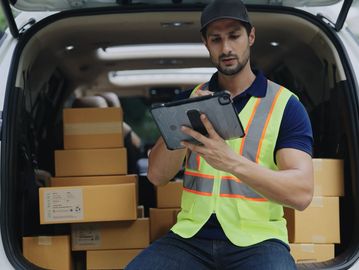 Delivery worker checking tablet with packages in van.