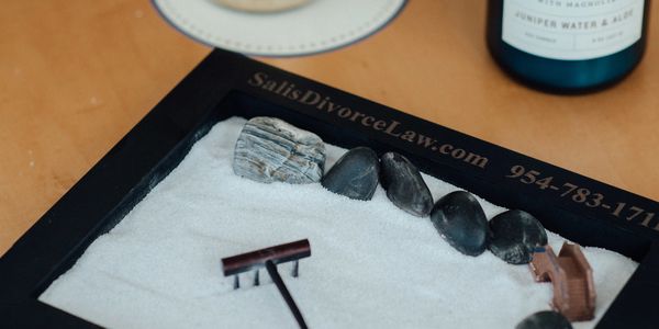 A miniature zen garden with white sand, black stones, and a small rake on a wooden table.
