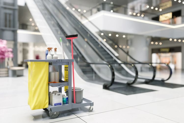 Cleaning cart with supplies in front of escalators inside a mall.