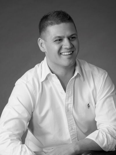 Young man in a white shirt smiling against a plain background.
