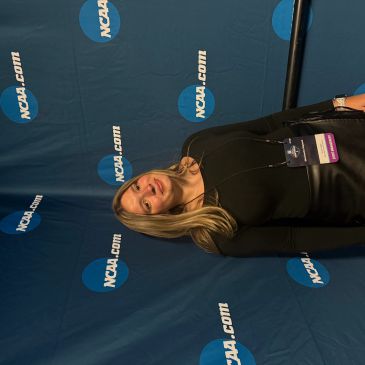 A young woman standing in front of an NCAA.com backdrop, smiling.