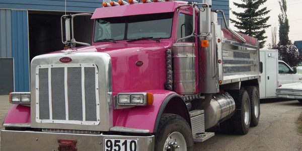 A bright pink dump truck parked outdoors near a building.