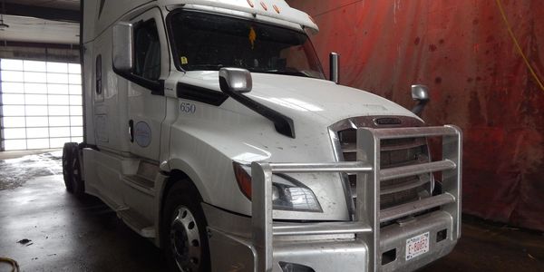 White semi-truck parked inside a garage with metal grille guard.