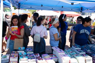 People browse books at an outdoor market under blue tents.