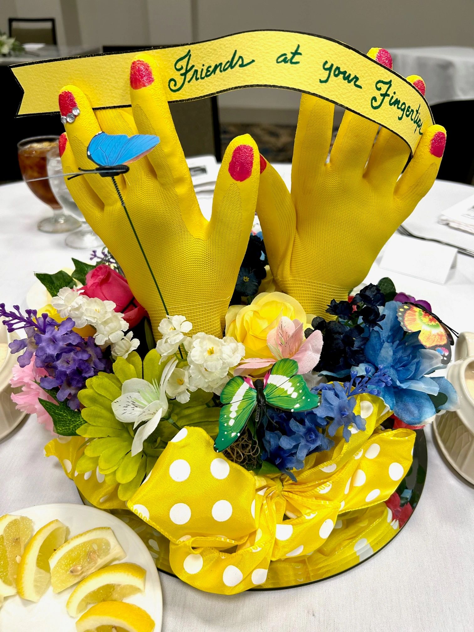 Yellow gloved hands with red fingertips and floral decorations on a table centerpiece.