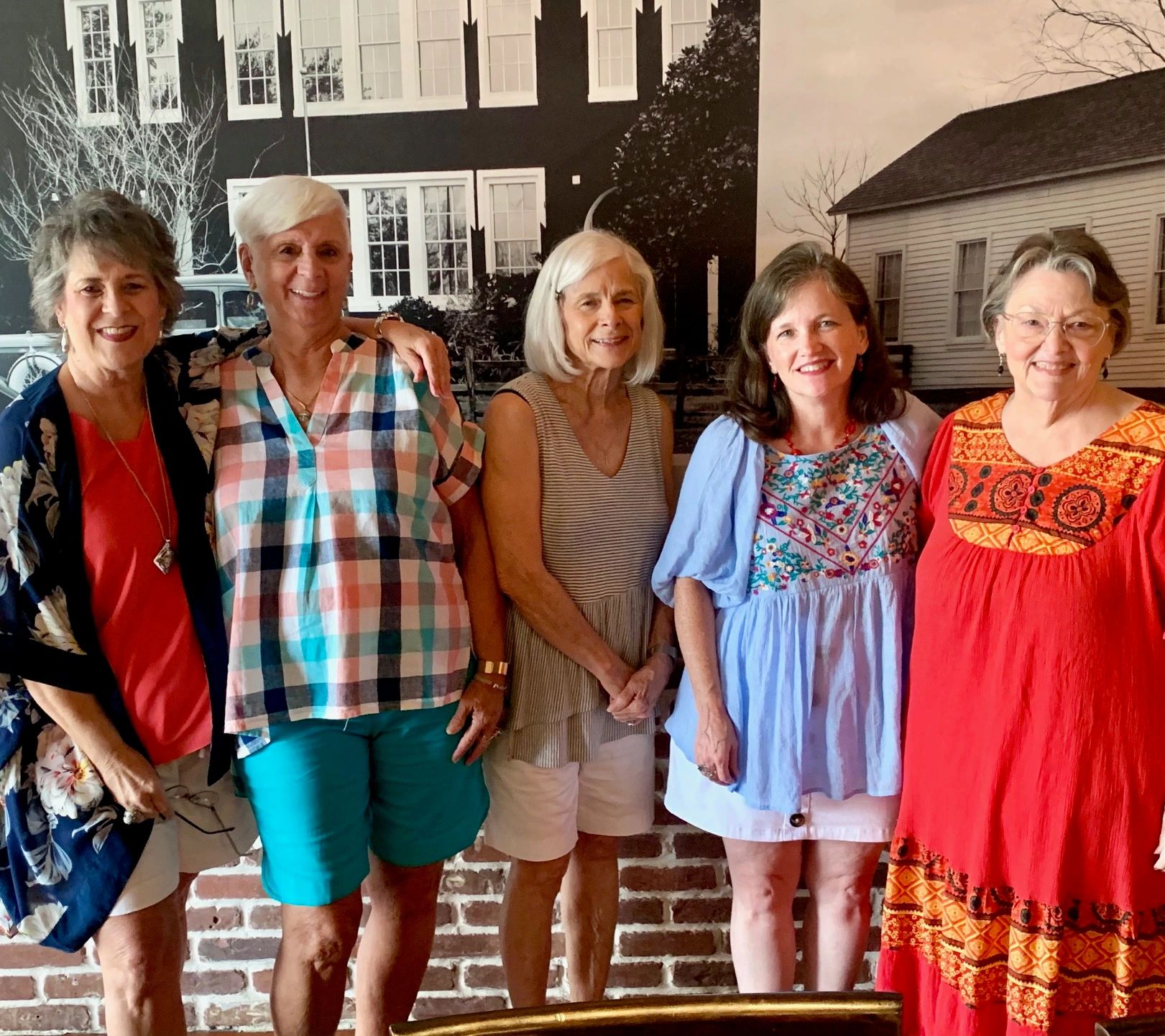 Five smiling women standing in front of a vintage black and white house backdrop.
