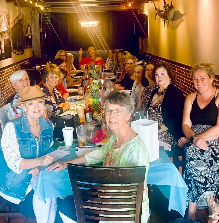 A large group of women gathered around a long table in a warmly lit restaurant.