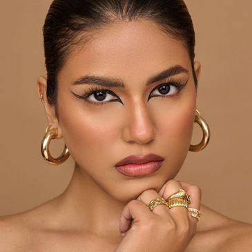 Close-up of woman with bold eye makeup and gold jewelry.