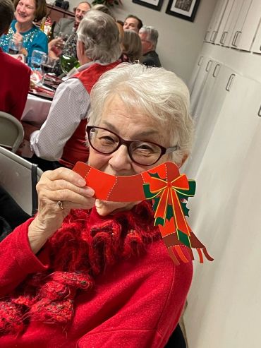 Elderly woman in red holding a festive holiday decoration and smiling.