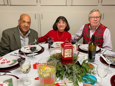 Three people seated at a holiday-themed dinner table with drinks and decorations.