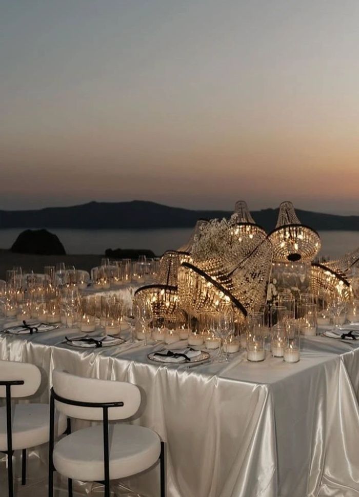 Elegant outdoor dinner setup with satin tablecloth and glowing chandeliers at sunset.