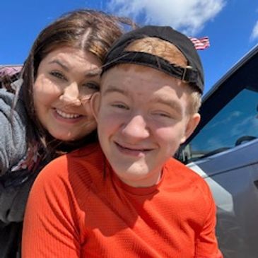 A woman and a man smiling for a selfie. The man has a backwards baseball cap.