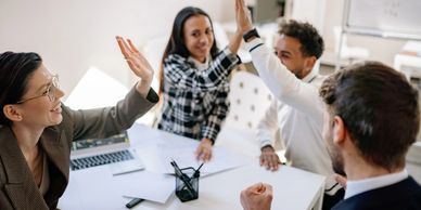 A group of four professionals are high fiving one another.