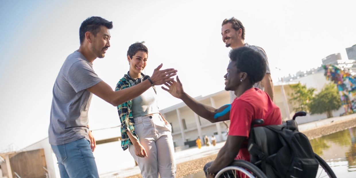 A group of four people, smiling. Two of them are high fiving. One is in a wheelchair.