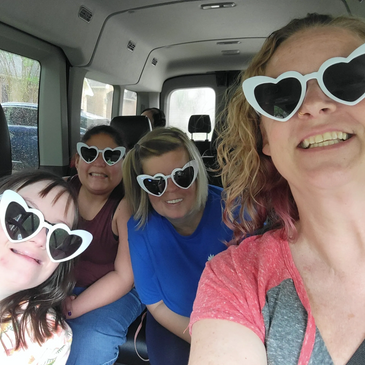 A group of women in a company vehicle. All of them are smiling and wearing heart-shaped sunglasses