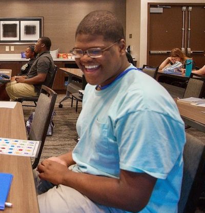 A high school boy is smiling big. He is playing some sort of a BINGO game in a conference room.