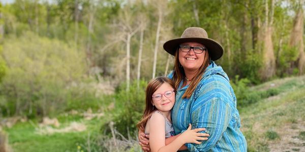 A woman and girl happily embracing outdoors in nature.