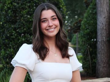 Smiling young woman in white dress outdoors.