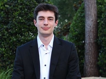 Young man in a black suit jacket outdoors.