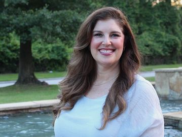 Smiling woman outdoors near water and trees.