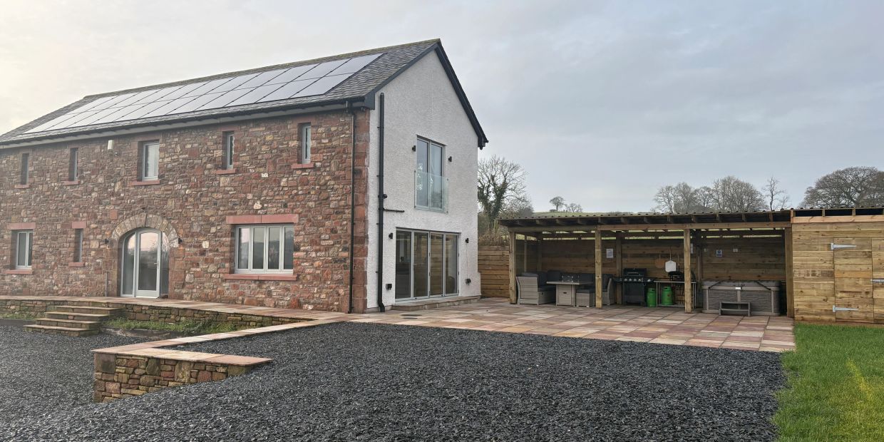 Stone house with solar panels and outdoor covered kitchen area.