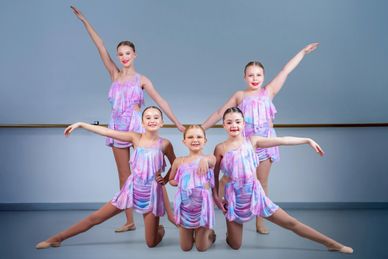 Five young dancers in pastel costumes pose gracefully in a studio.