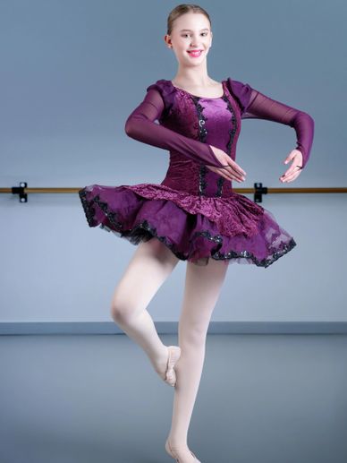 Ballet dancer in a purple costume poses gracefully in a studio.