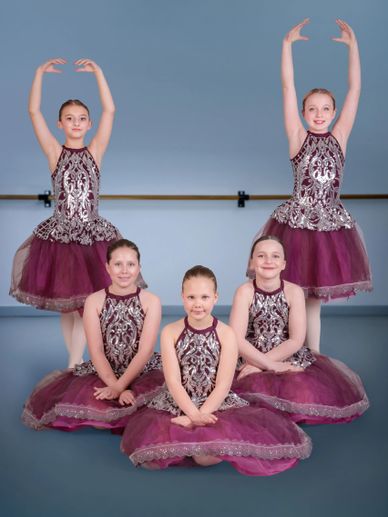 Five young ballerinas in matching purple and silver costumes posing gracefully.