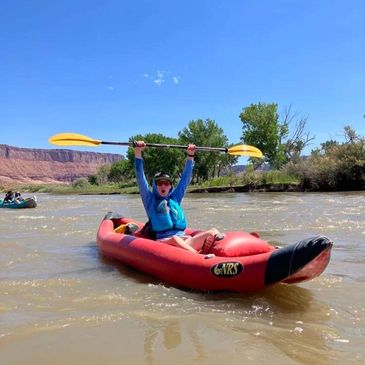 Person in kayak with his arms holding a paddle up and floating in a river in Moab Utah