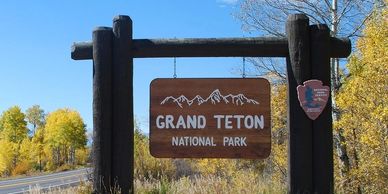Entrance sign for Grand Teton National Park surrounded by autumn trees.