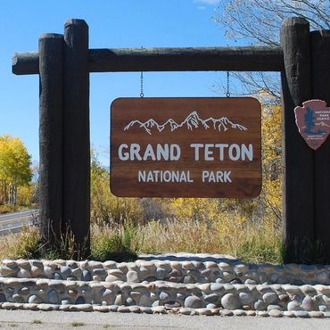 Entrance sign for Grand Teton National Park surrounded by autumn trees.