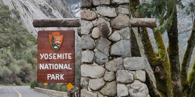 Entrance sign for Yosemite National Park on a stone pillar near a winding road.