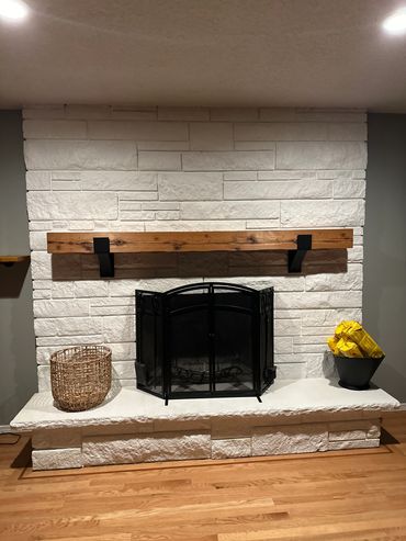 Rustic fireplace mantel on a stone wall with metal brackets. 
