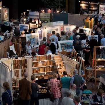 Crowded indoor art and craft fair with various displays and visitors.