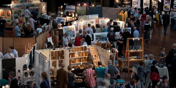 Crowded indoor art and craft fair with various displays and visitors.