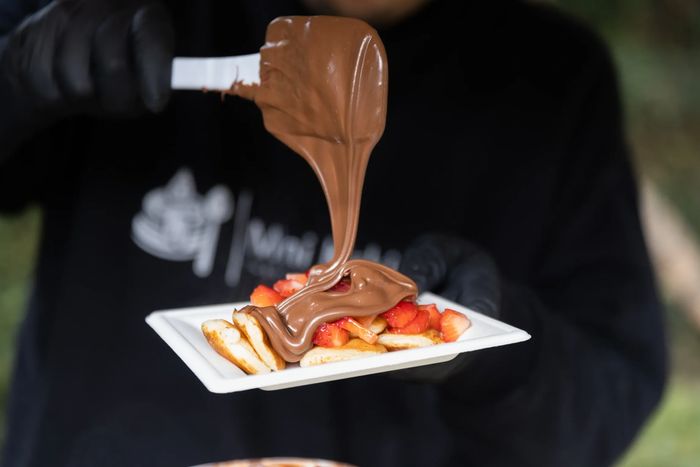 Pouring chocolate sauce over pancakes with strawberries.