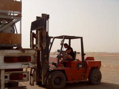 A man operates a forklift in a sandy, desert-like area during daylight.