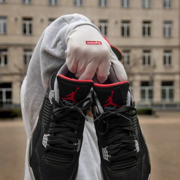 Pair of black Jordan shoes being held up by someone in front of a building.