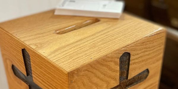 Close-up of a square wooden offering box with a slot in the top for donations and cross carvings