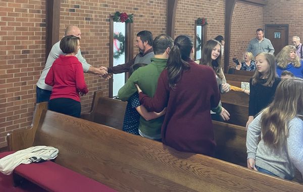 Church attenders standing and shaking hands, while some sit on pews, during the greeting time