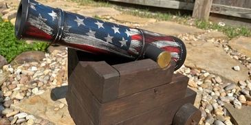 Decorative wooden cannon painted with the American flag on a stone patio.