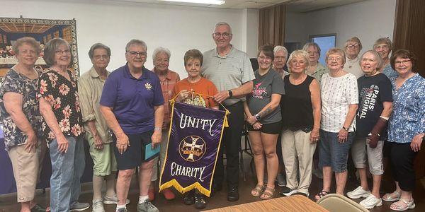 Group of people holding a Unity Charity banner in a meeting room.