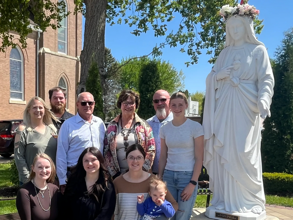 Group of people posing beside a statue of a woman with a flower crown.
