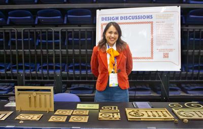 Woman stands behind a table displaying wooden design pieces at a design discussion event.