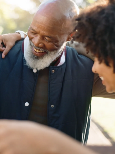 Joyful elderly man with white beard smiling and hugging others outdoors.