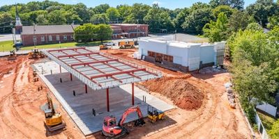 Construction site with steel framework and machinery on dirt ground.