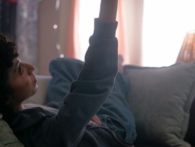 Person lying on a couch reaching up.