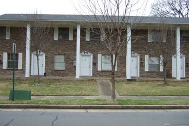 Row of brick townhouses with white doors and small trees in front.