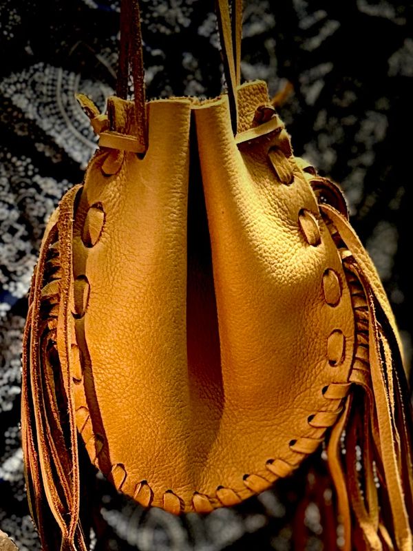 Handcrafted leather pouch with fringe details hanging against a patterned background.