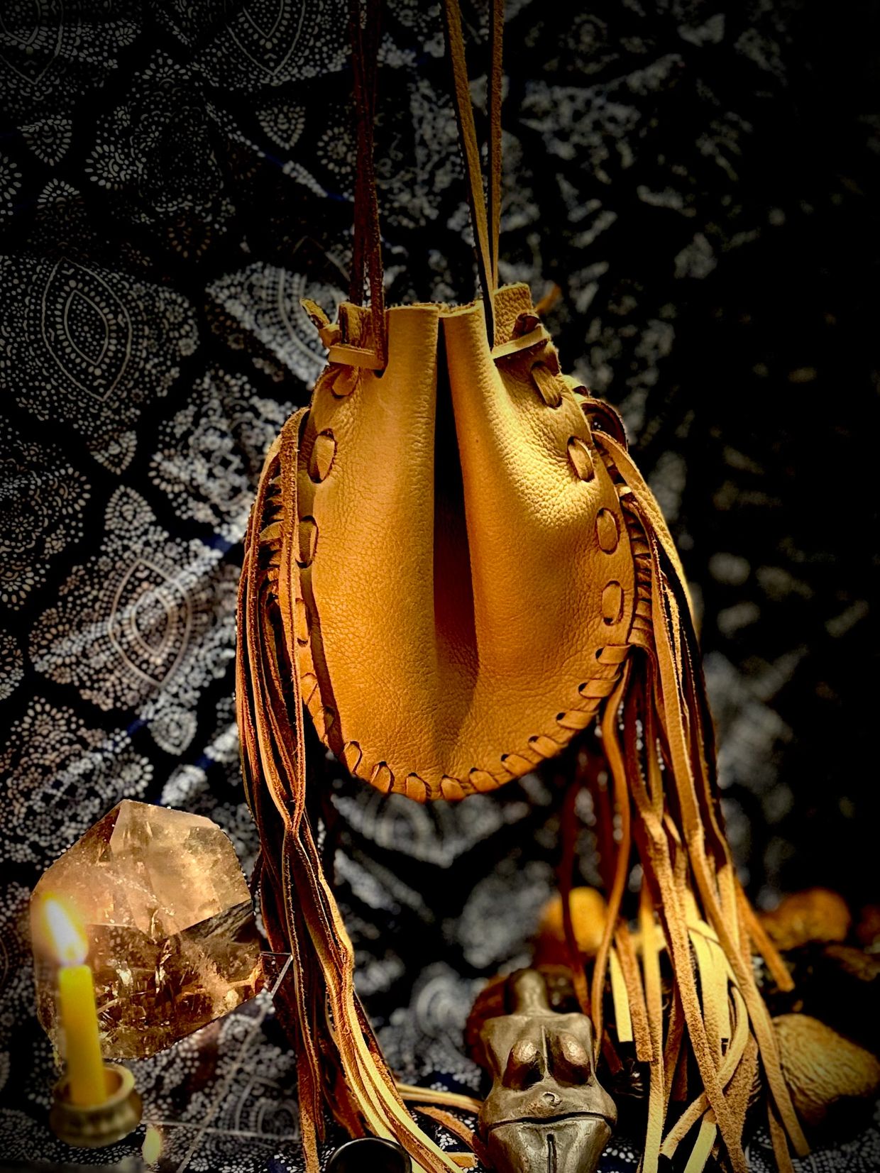 Handcrafted leather pouch with fringe details hanging against a patterned background.